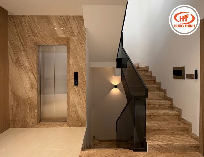 Thang máy và cầu thang ốp đá Marble Vân Gỗ Ý phối sàn nhà tông be nhẹ.