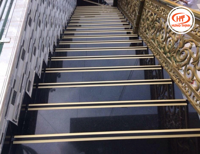 Đá tự nhiên ốp cầu thang màu đen kết hợp với đường chỉ và lan can vàng tạo sự nguy nga lộng lẫy